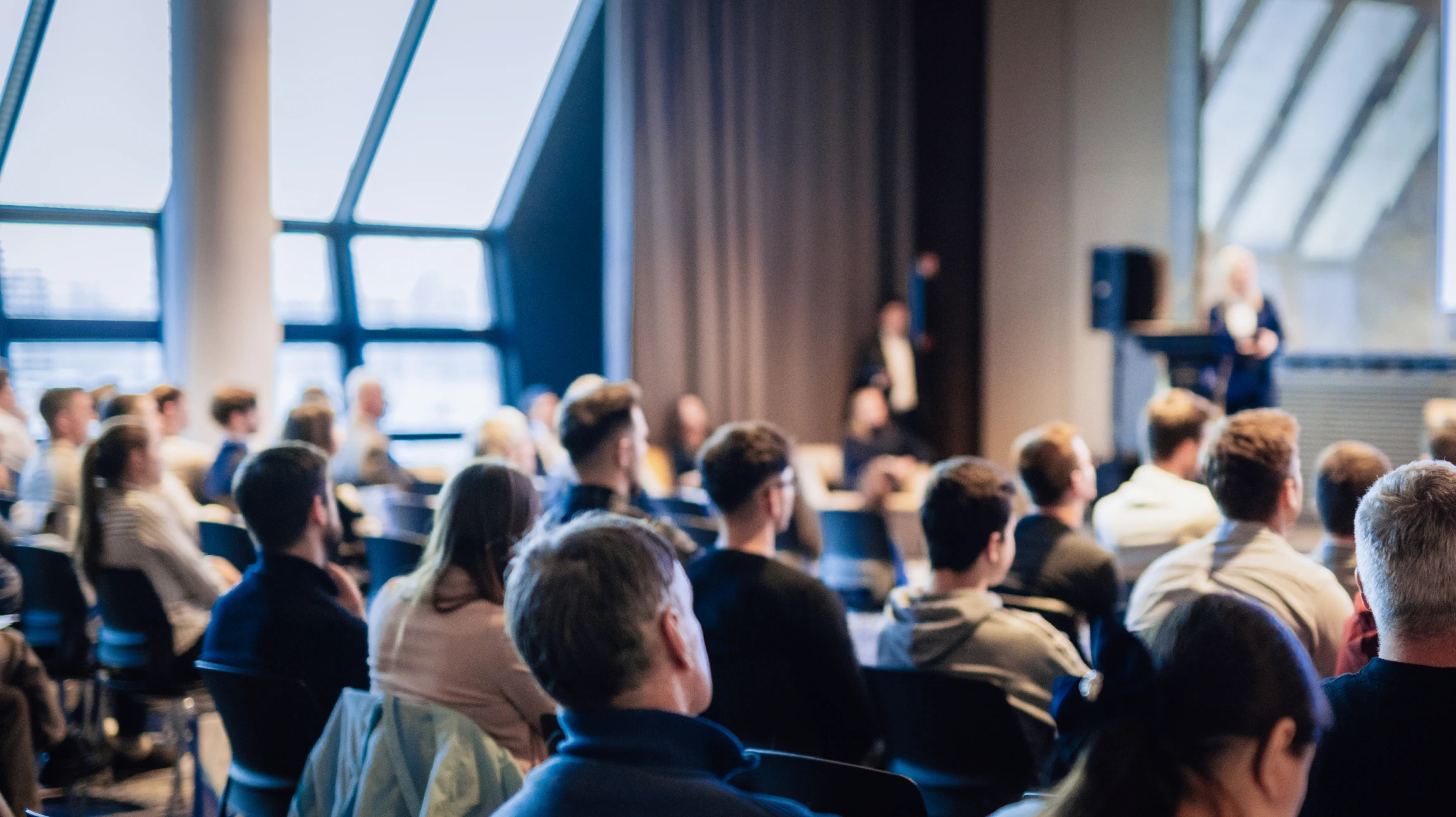 Salle de conférence moderne avec un formateur en chemise bleue présentant devant un public assis